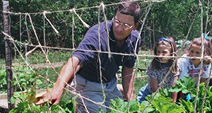 an adult volunteer talks to two school aged children about garden plants