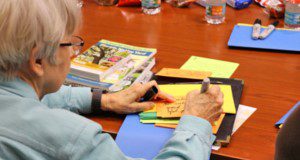 person seated at a conference table with markers and construction paper, filling out a data card during a journey-mapping session