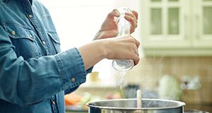 woman's hands using salt grinder over a steaming cookpot