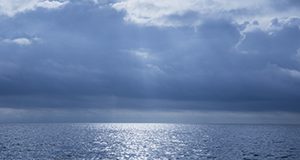 Photo of striking clouds over the Gulf of Mexico showing the horizon and rays of sun coming through the clouds turning the water silver.