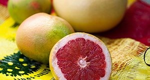 A photo of a halved red grapefruit and other whole grapefruits in the background, all on a Florida citrus bag.