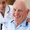 An old man sitting with a nurse behind him.