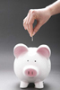 A hand holding a coin above a piggy bank.