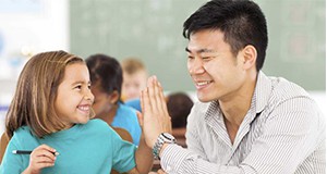 A photo of seated child and adult exchanging a high-five in an elementary school classroom.